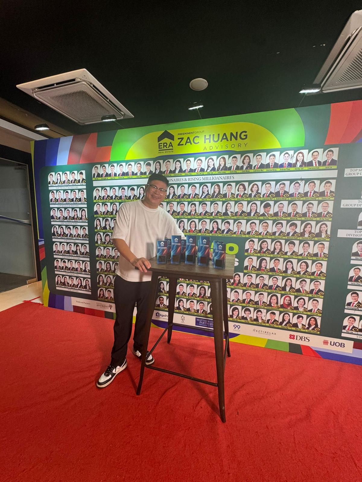 Christopher beside the Zac Huang Advisory Millionaires wall with trophies