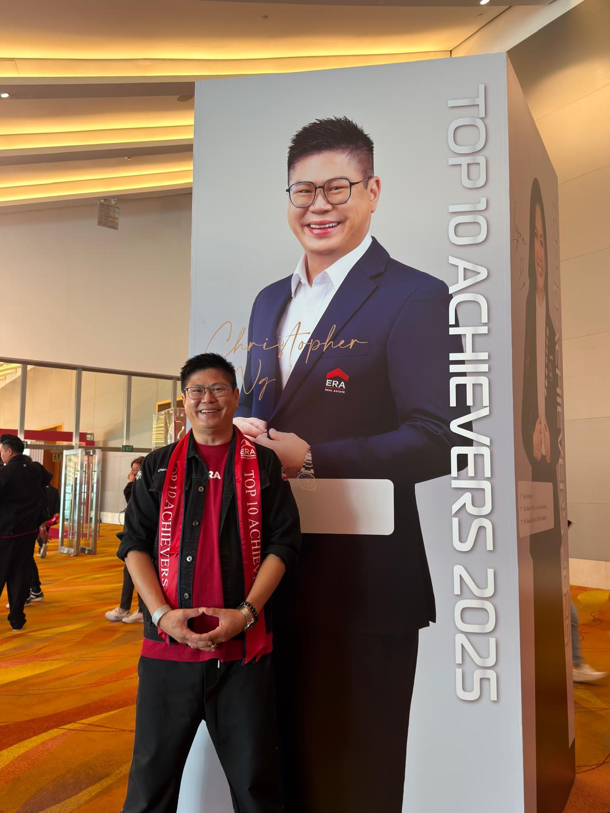 Christopher beside Top 10 Achievers 2025 standee at ERA APAC